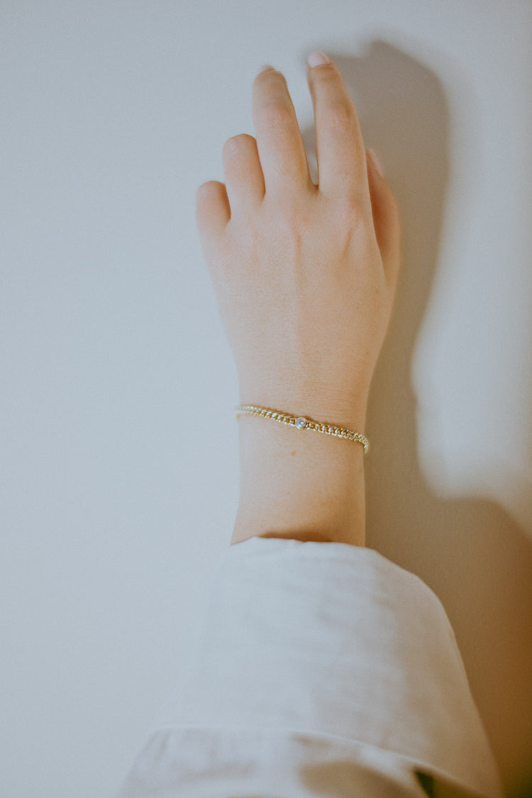 Hand wearing a recycled gold bracelet with a round natural white diamond on a light background