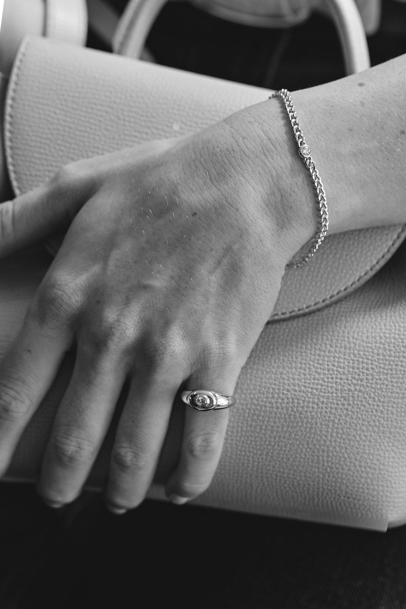 Close-up of a hand holding a textured clutch with a ring and bracelet with one natural unique oval white diamond.