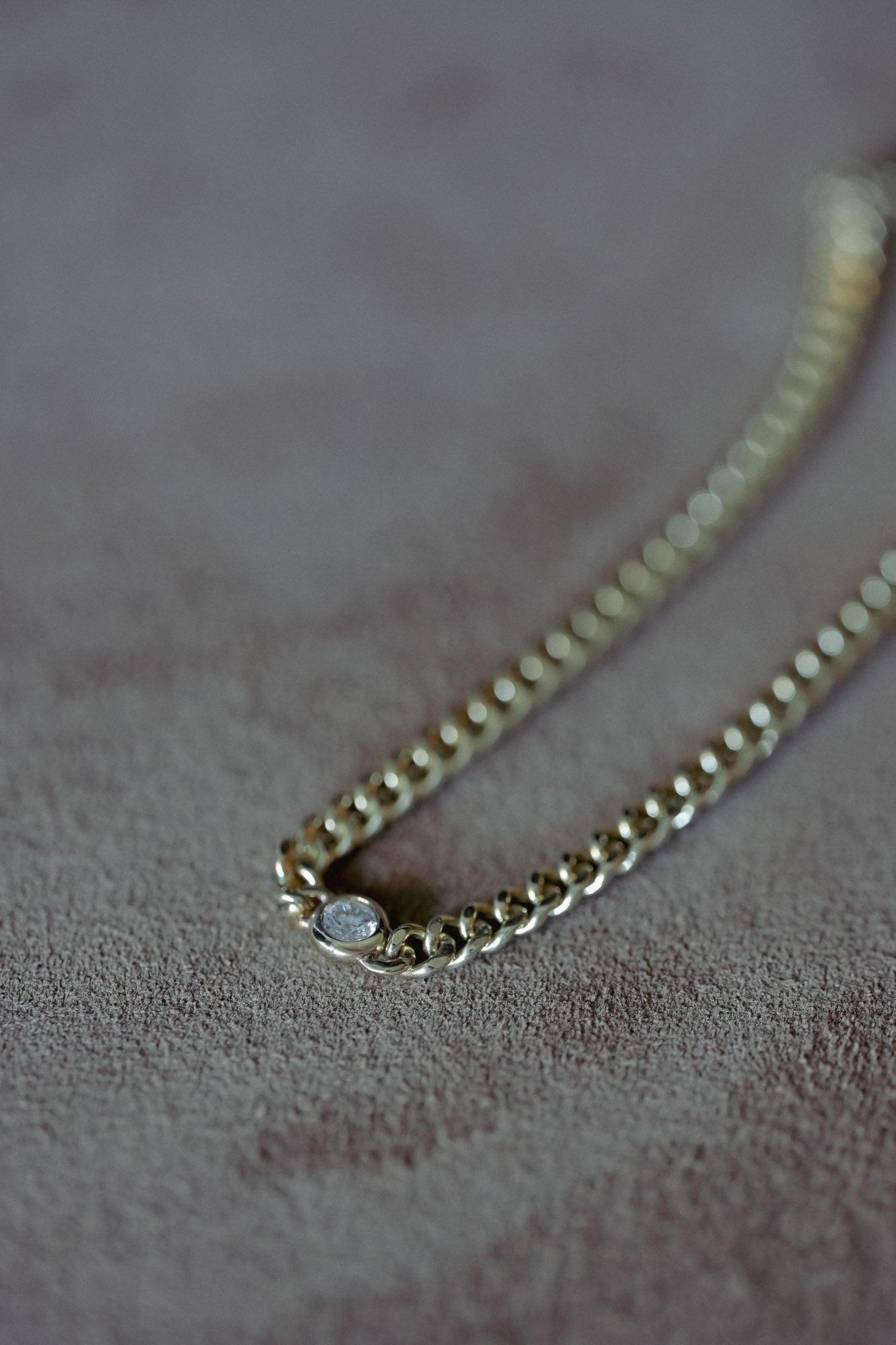 Gold chain bracelet with a round natural white diamond on a textured surface. Ethically sourced