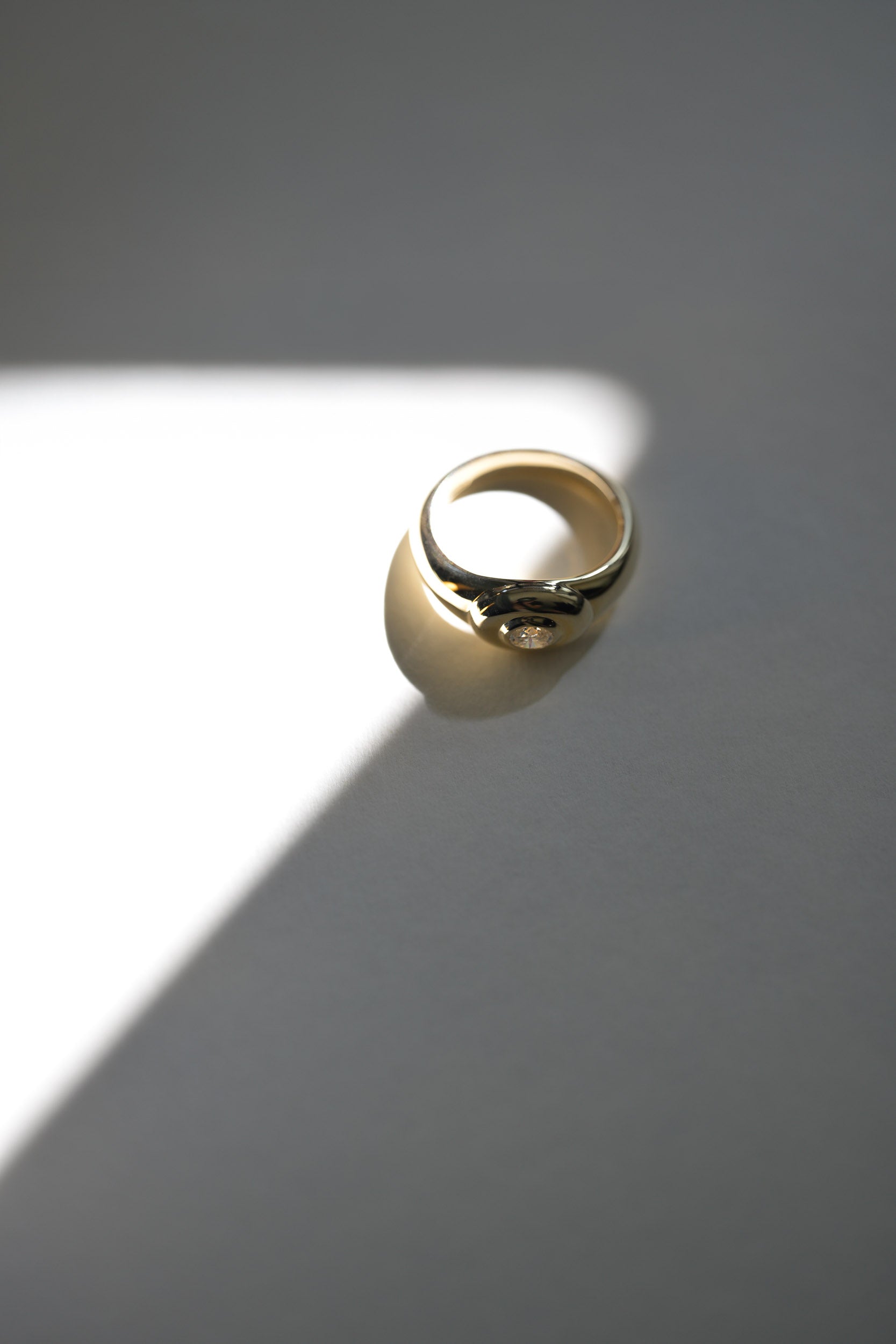 Gold signet ring on with a oval natural diamond on a gray surface with a soft shadow