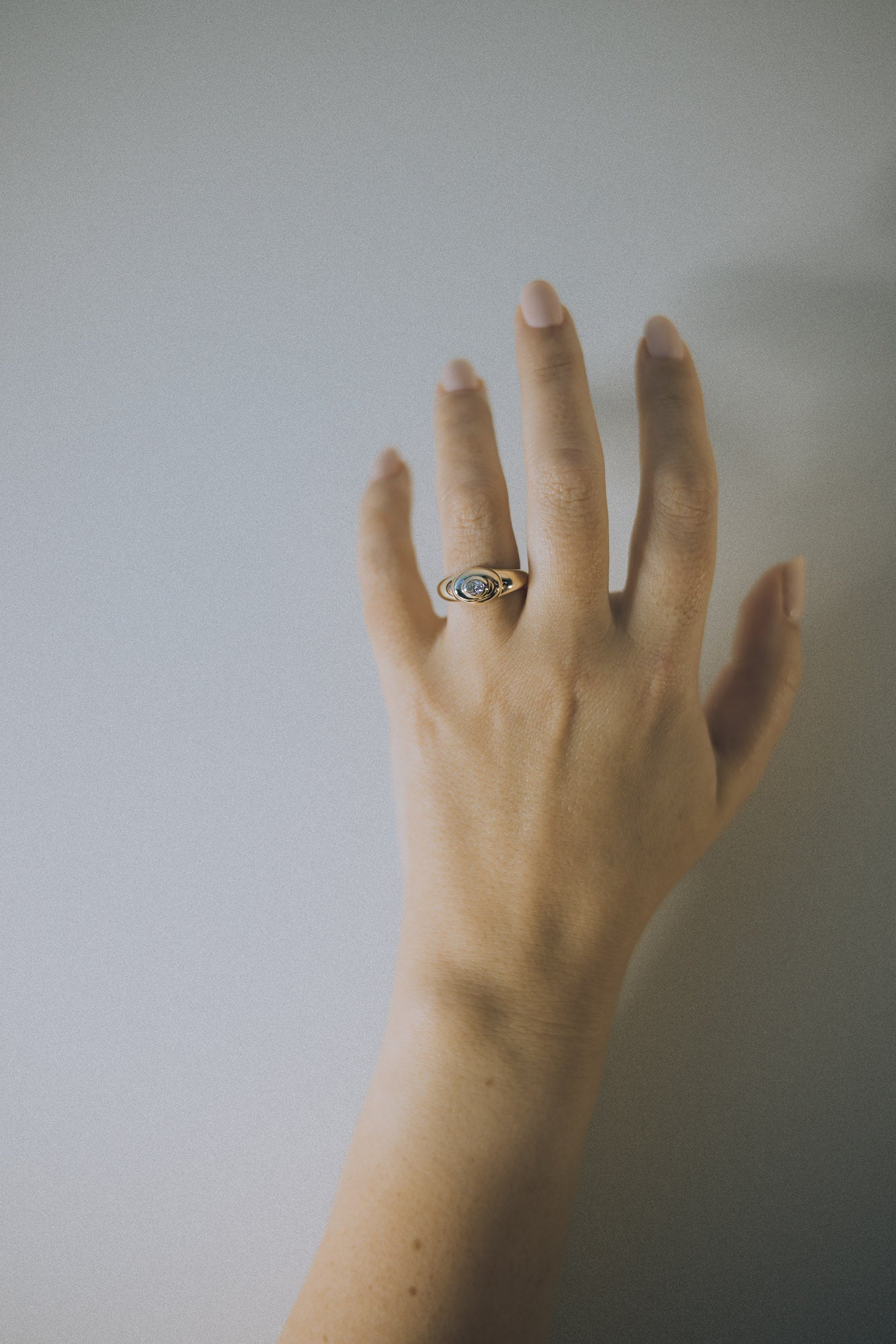 Hand wearing a signet ring with a oval diamond on a plain background