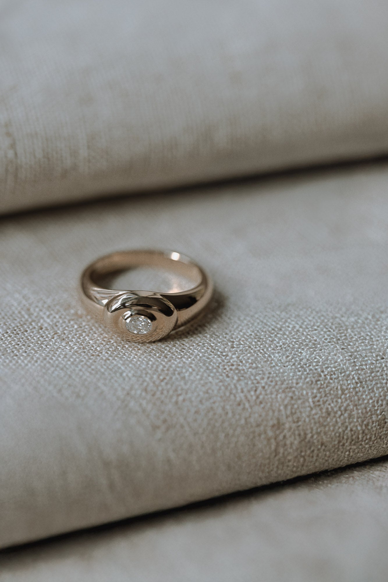 Modern signet ring with a oval diamond on a textured beige surface