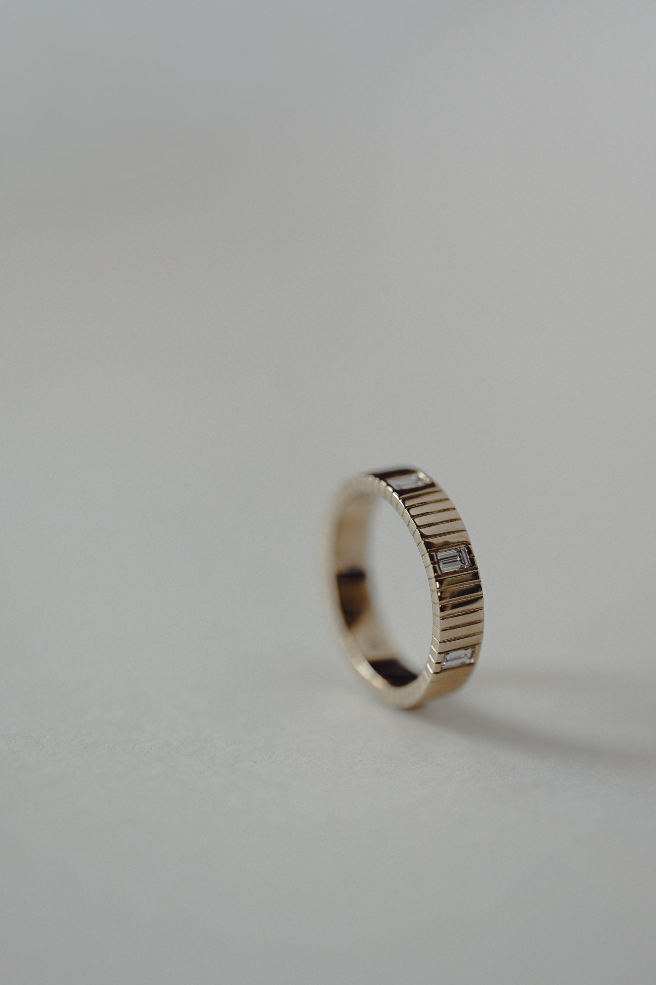 Gold ring with recycled baguette diamond with a textured band on a gray background
