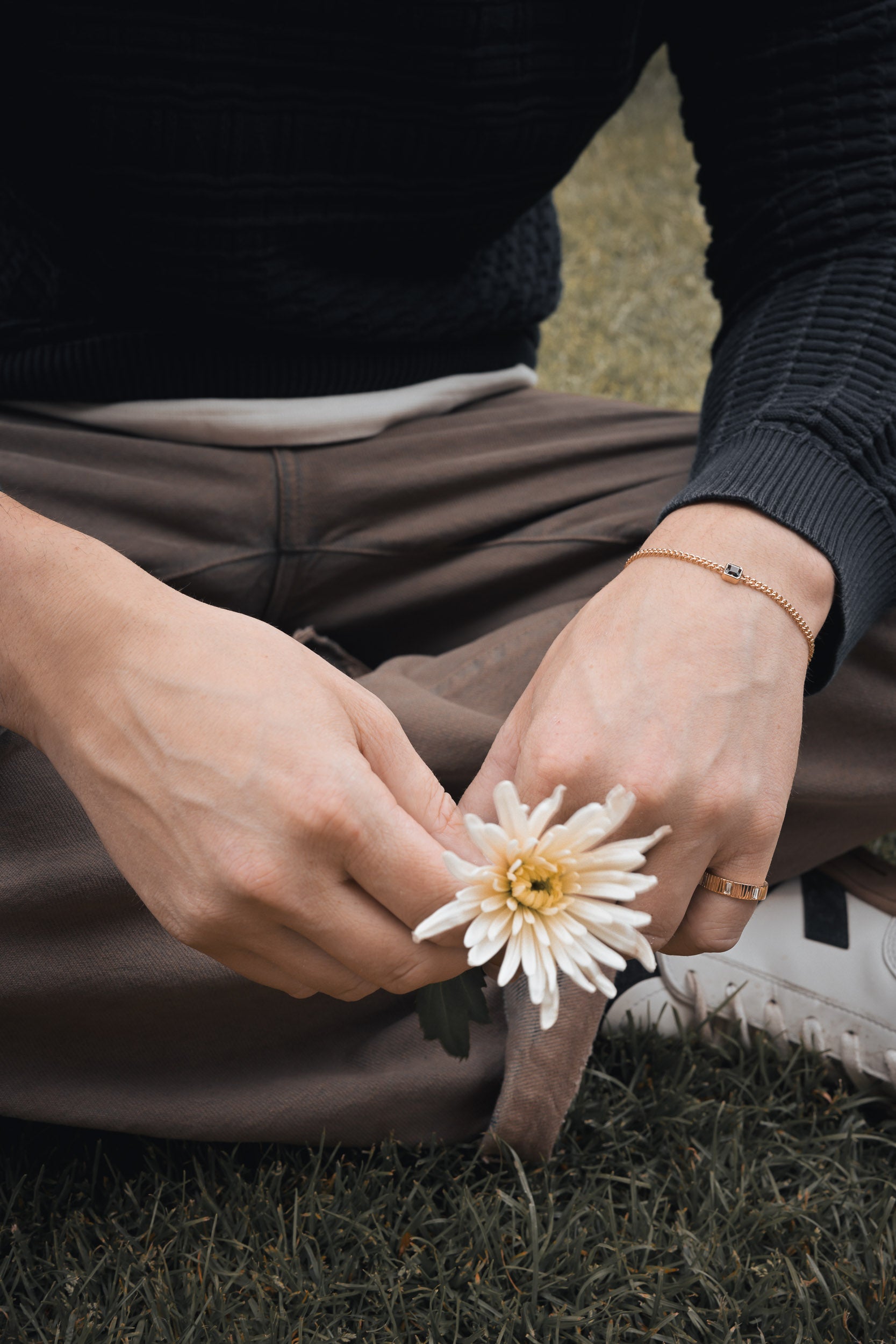 Person holding a white flower on grass featuring a recycled gold sapphire bracelet