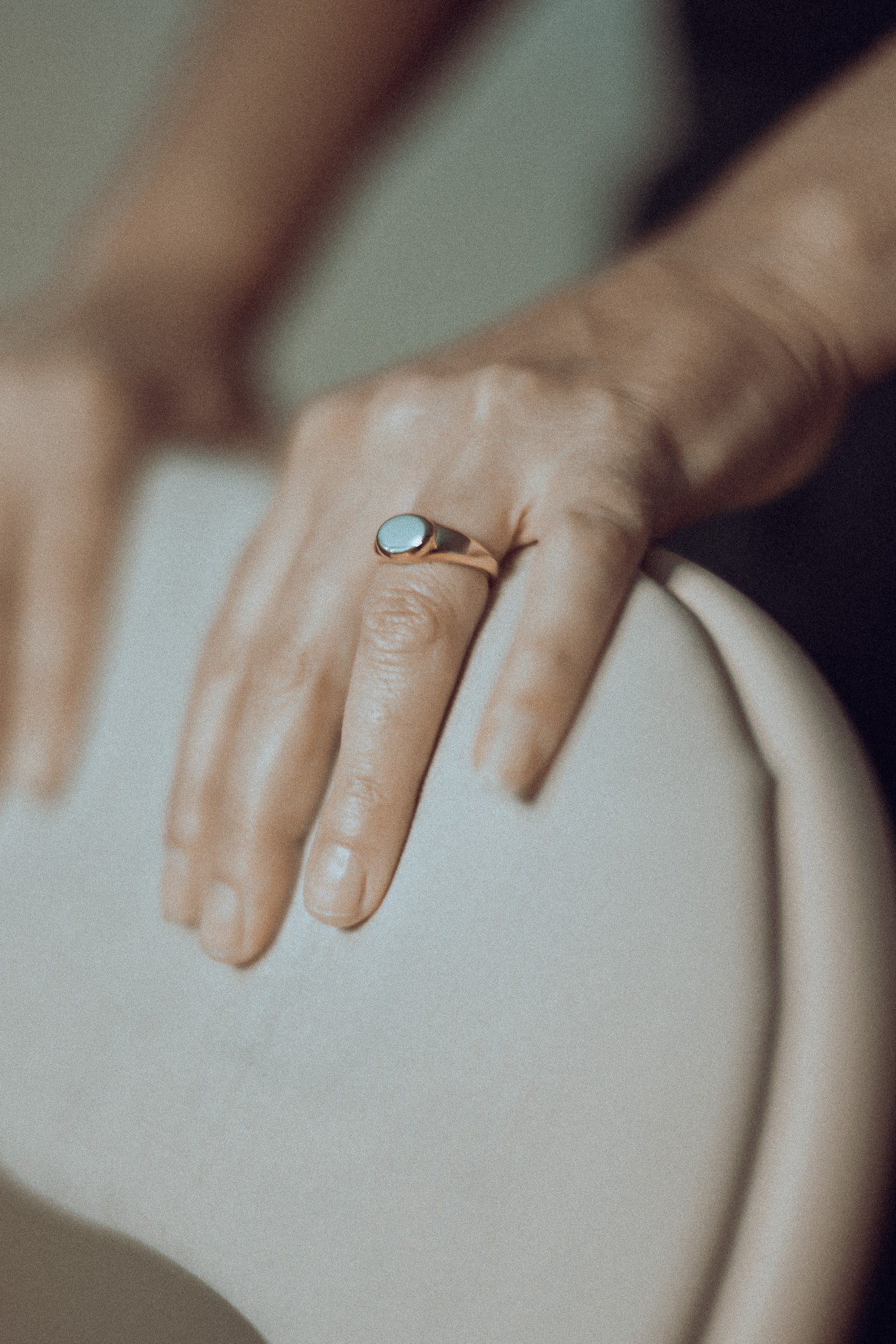 Close-up of a woman hand wearing a timeless signet ring on a blurred pink background