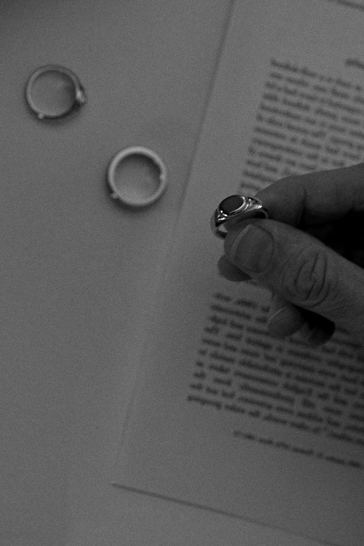 Close-up of a hand holding a timeless signet ring over a piece of vintage newspaper