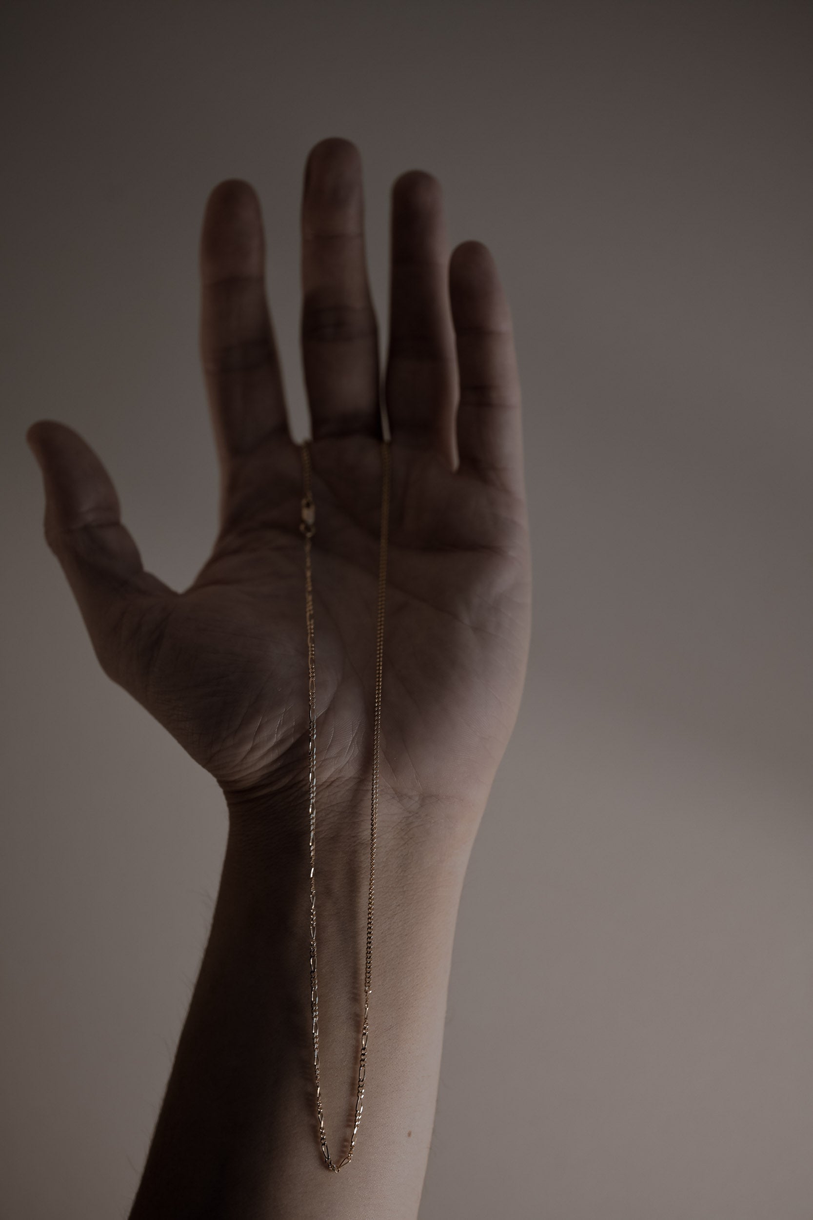 Hand showcasing a delicate gold chain with unique design against a neutral background
