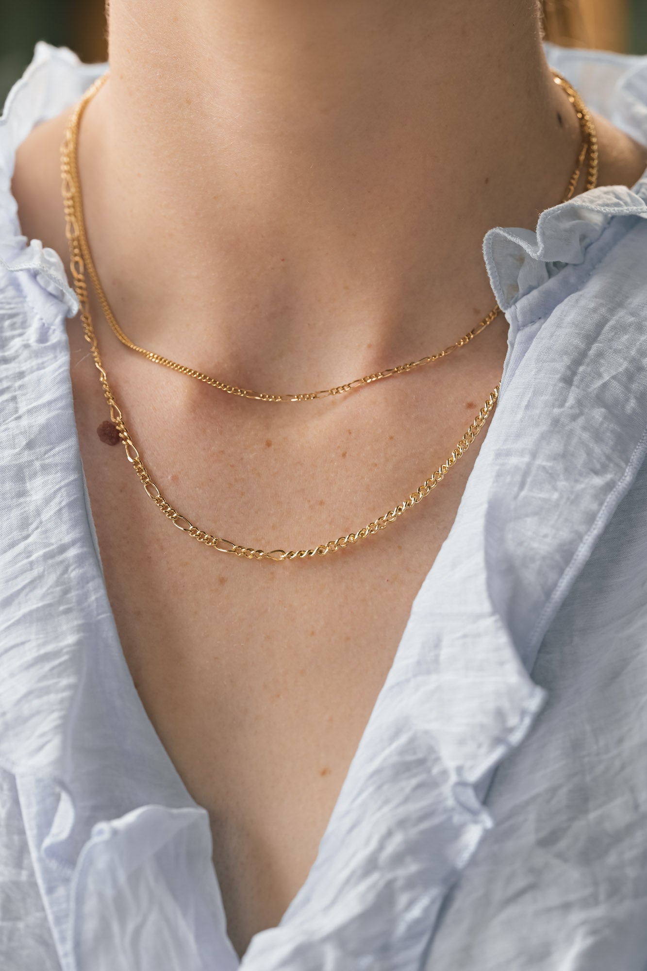 Close-up of a woman wearing gold the different necklaces options with a white blouse.