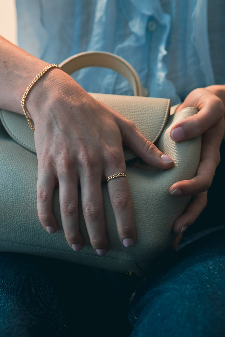 Close-up of hands holding a coloured clutch with a rope style ring made in London. 