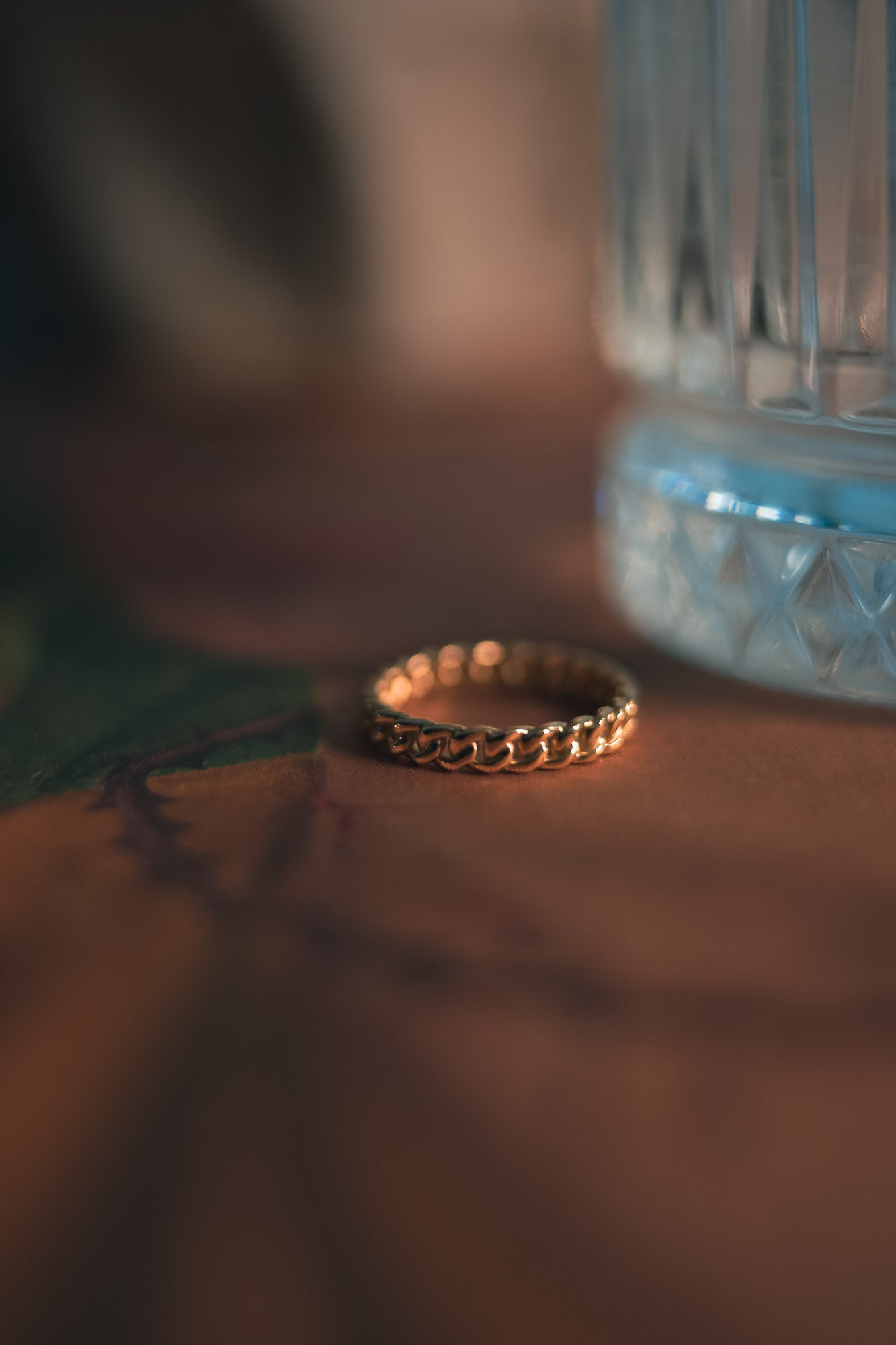 Gold curb style ring on a textured surface with a blurred background