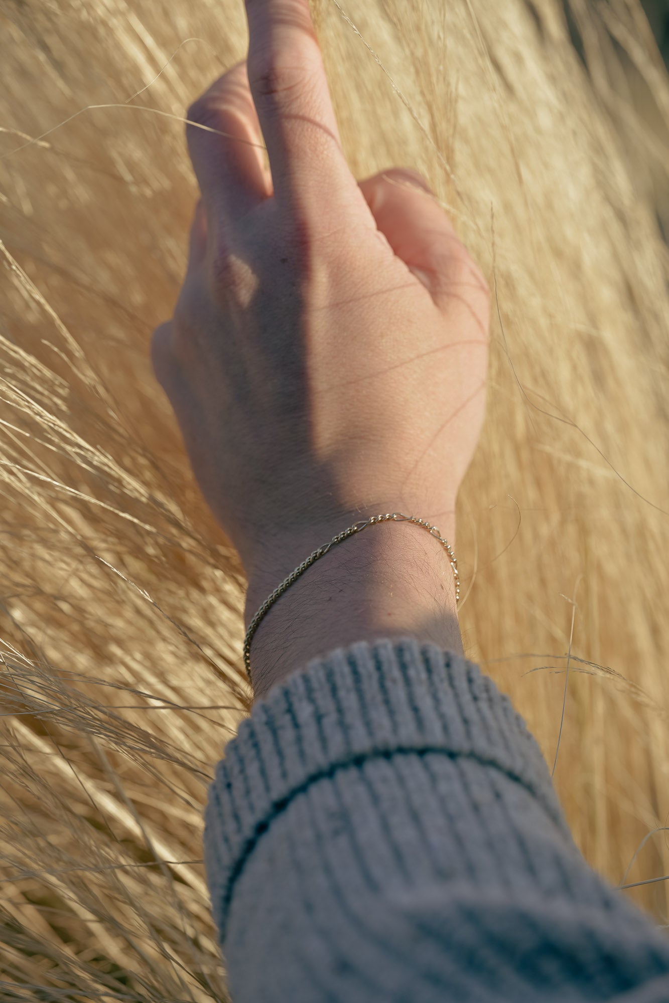 Hand with a one-of-a-kind gold bracelet touching dry grass
