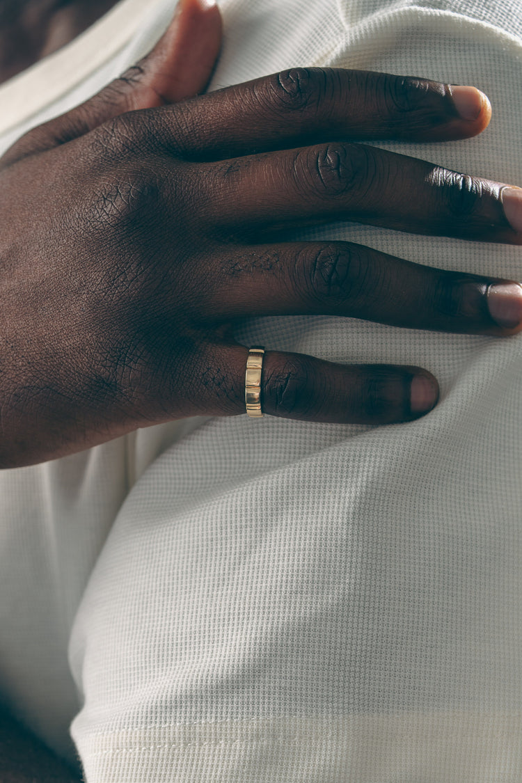 Hand with a gold architectural modern ring  band on a white fabric background