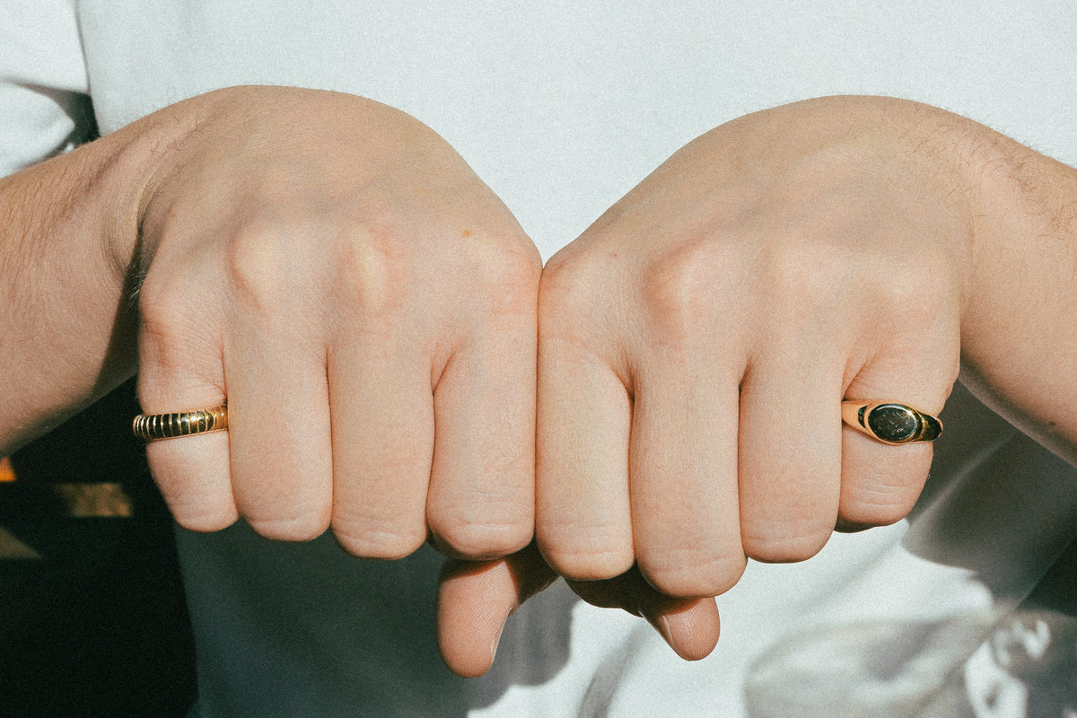 Two hands wearing recycled gold rings with blurred background