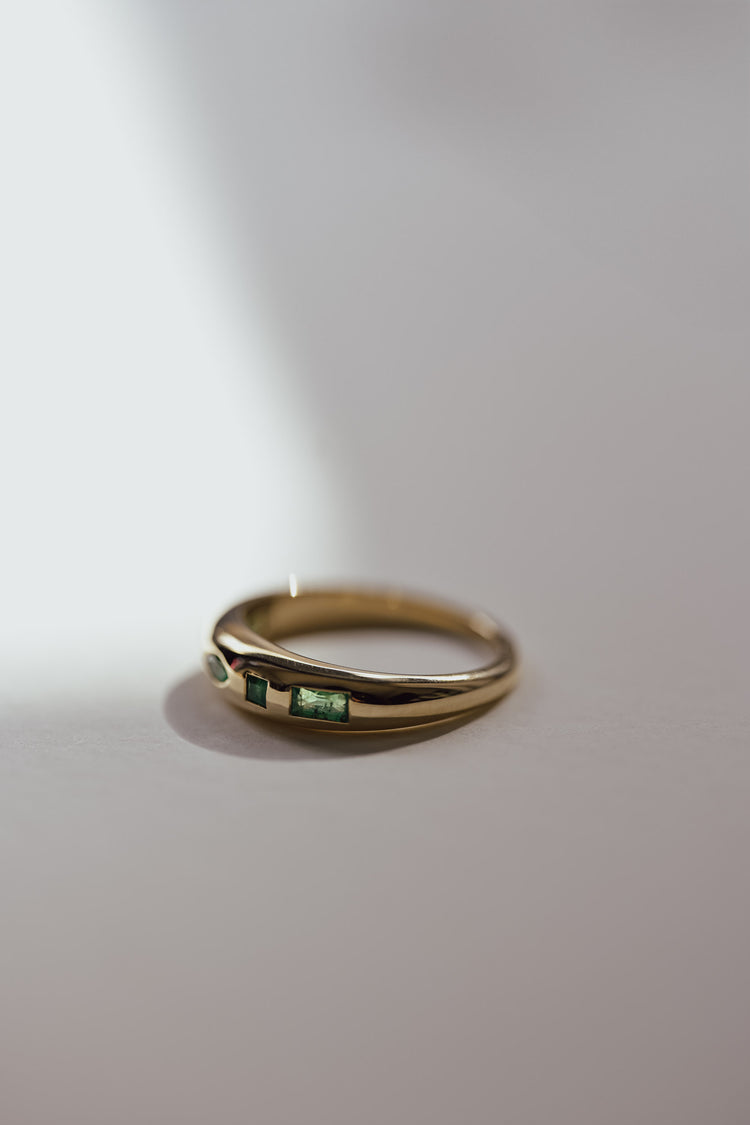 Gold ring with embedded green gemstones on a light gray background