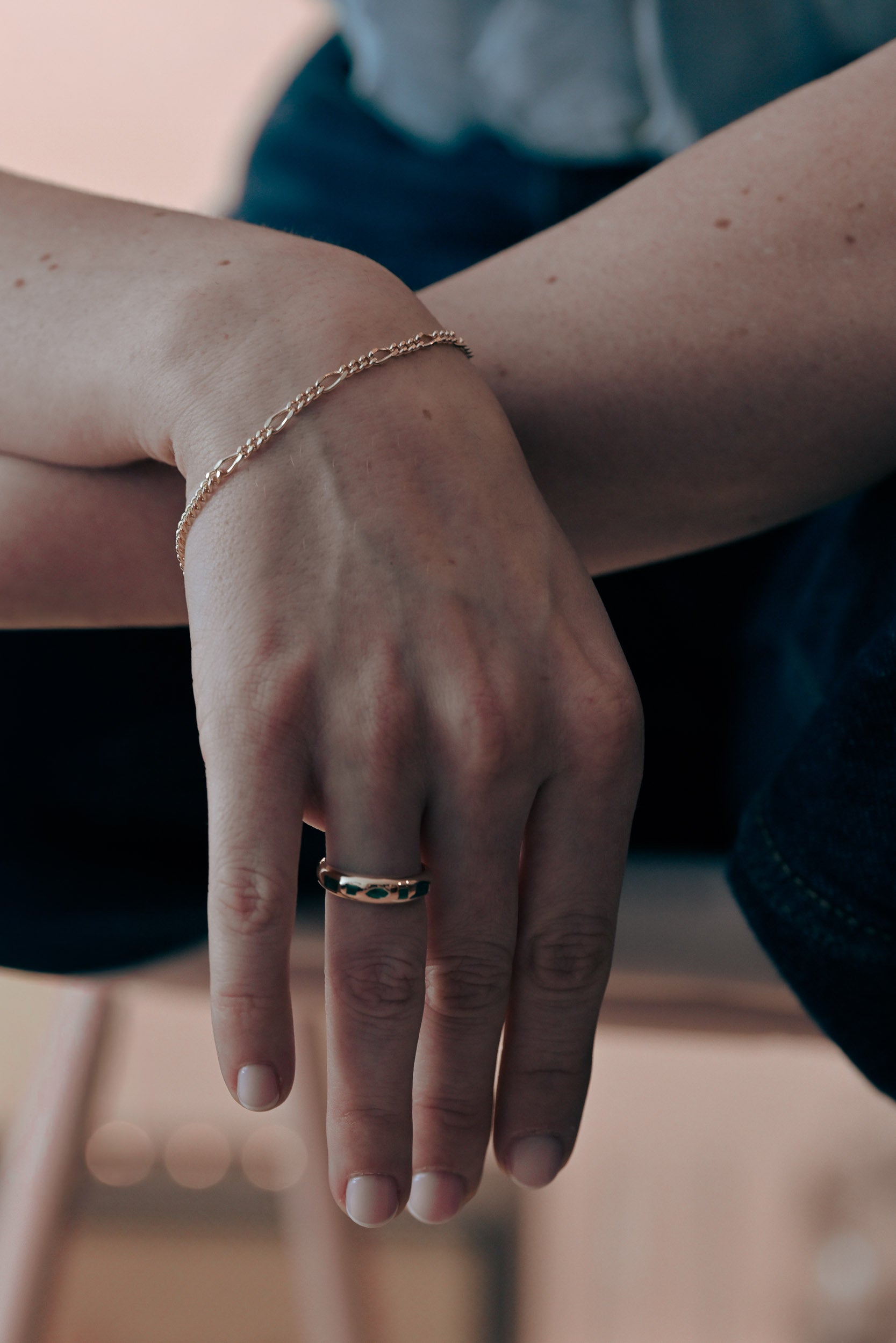 Close-up of a hand with a gold bracelet and ring with emeralds on a blurred aesthetic background