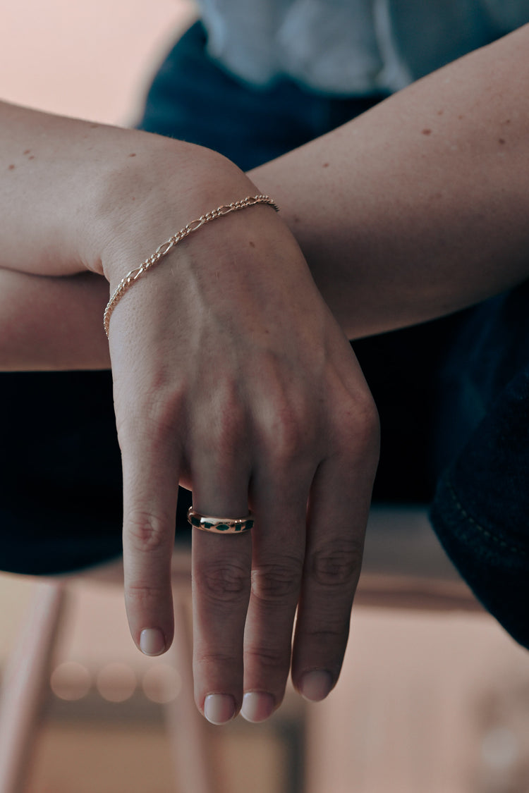 Close-up of a hand with a gold bracelet and ring with emeralds on a blurred aesthetic background