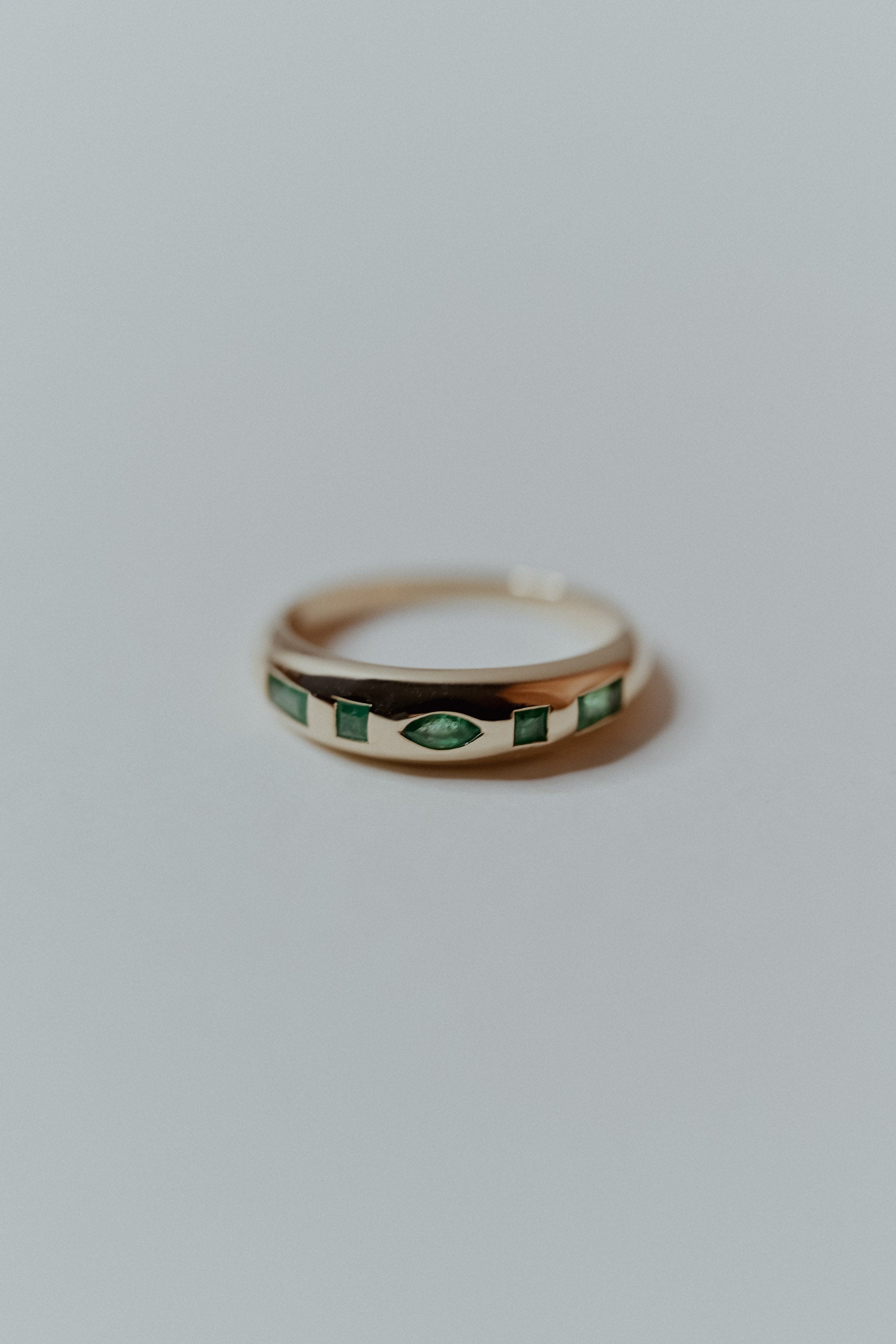 Gold ring with green emerald natural gemstones on a light gray background