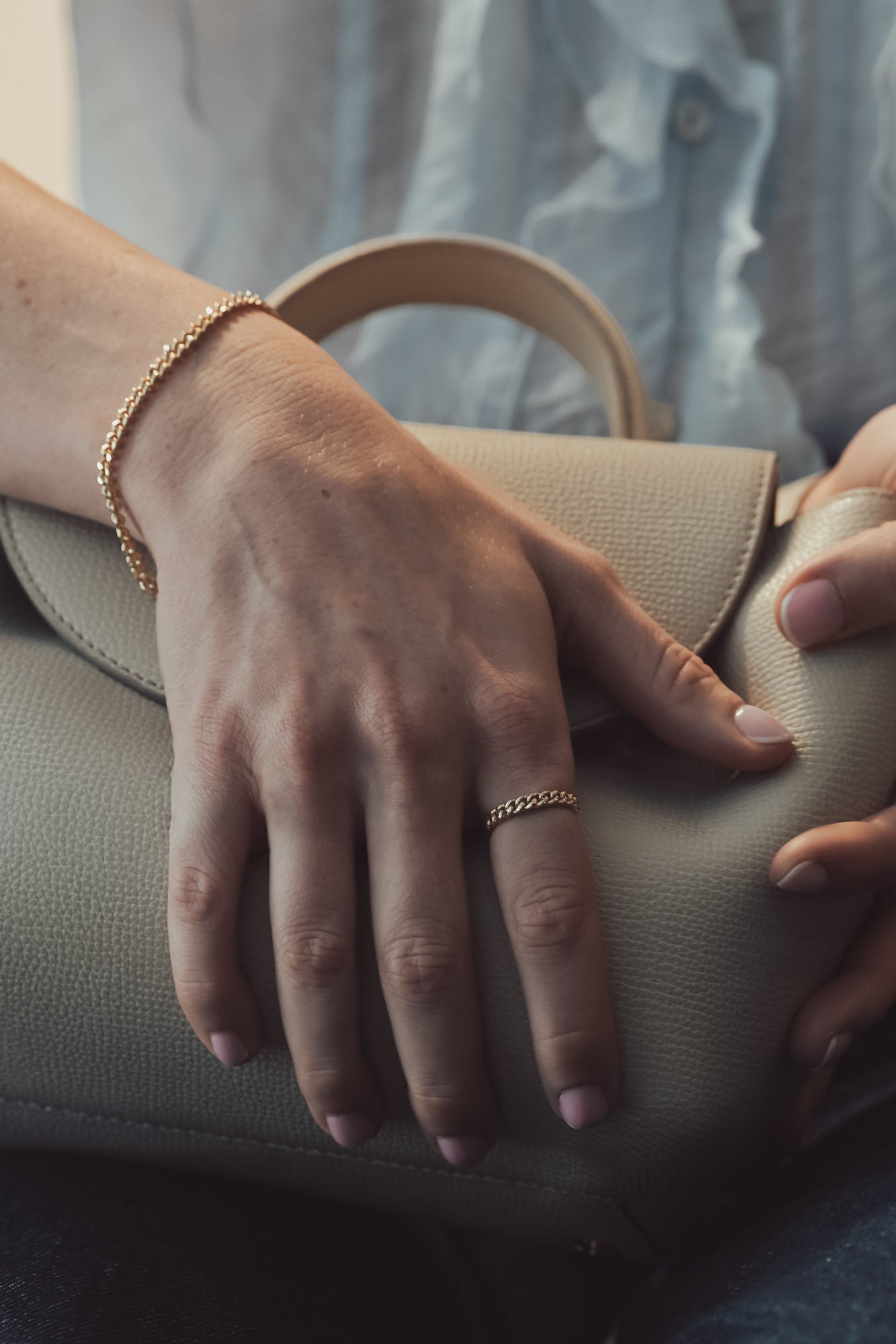Close-up of a curb chain bracelet holding a beige clutch with a blurred background