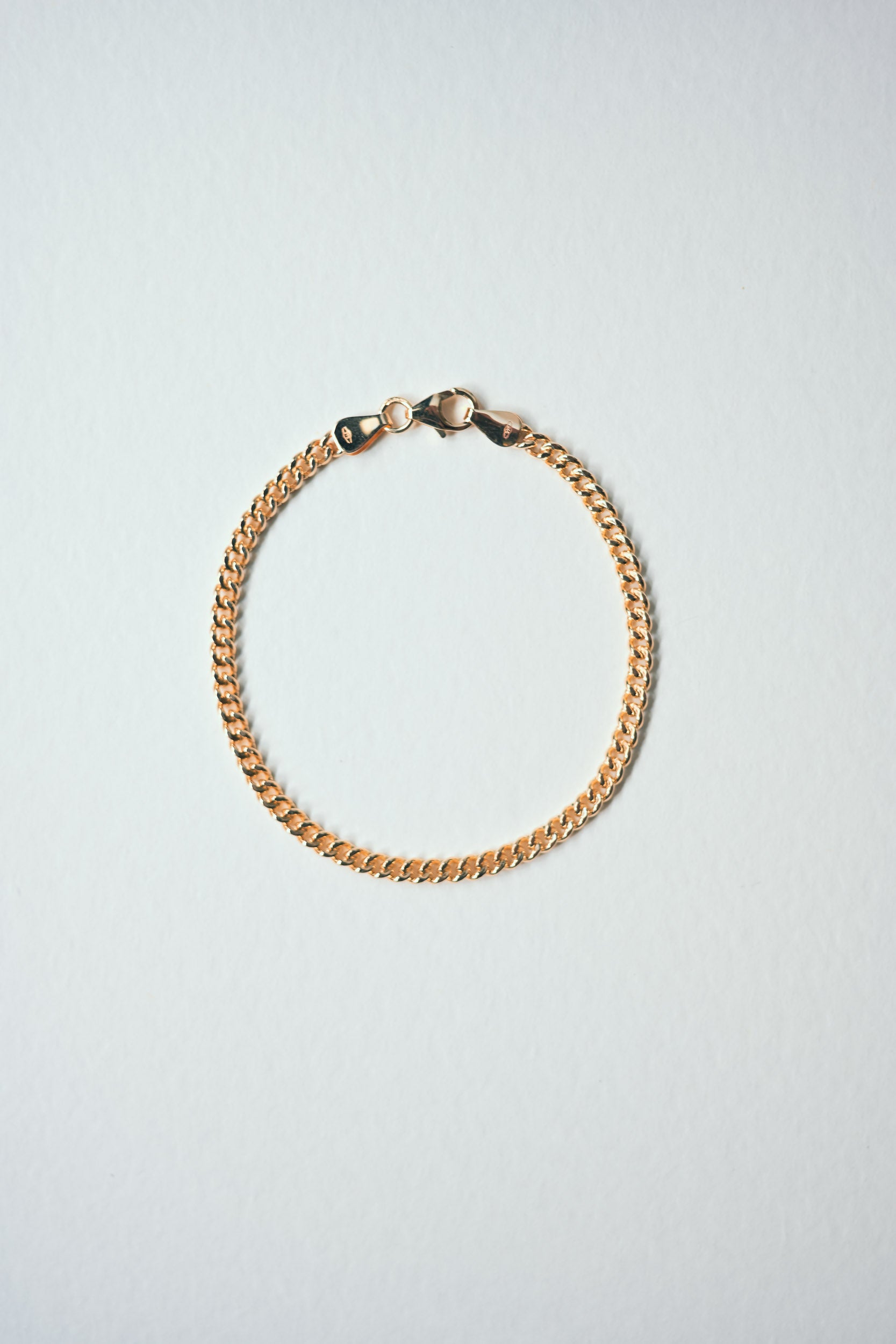 Gold chain bracelet curb styled on a light grey background, quiet luxury made in London