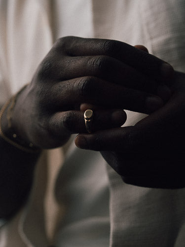 Close-up of two hands holding a gold ring against a neutral background