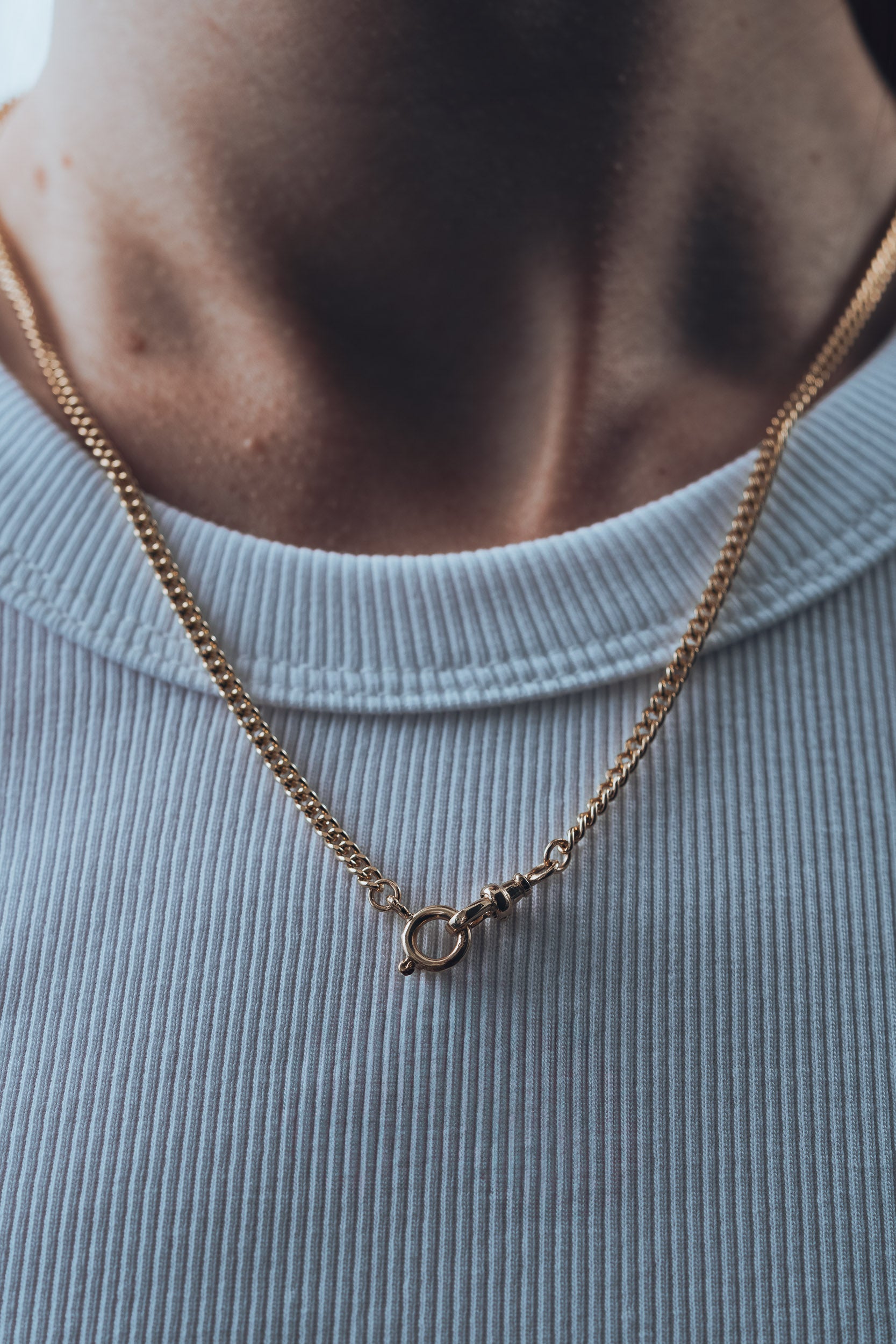Gold chain necklace with a t bar pendant on a person wearing a light blue shirt